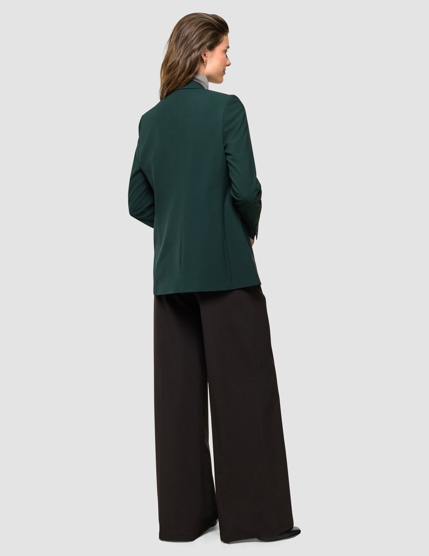 Ease Blazer Reg i Evergreen, helfigur bagfra af kvinde i mørkegrøn blazer og sorte bukser.